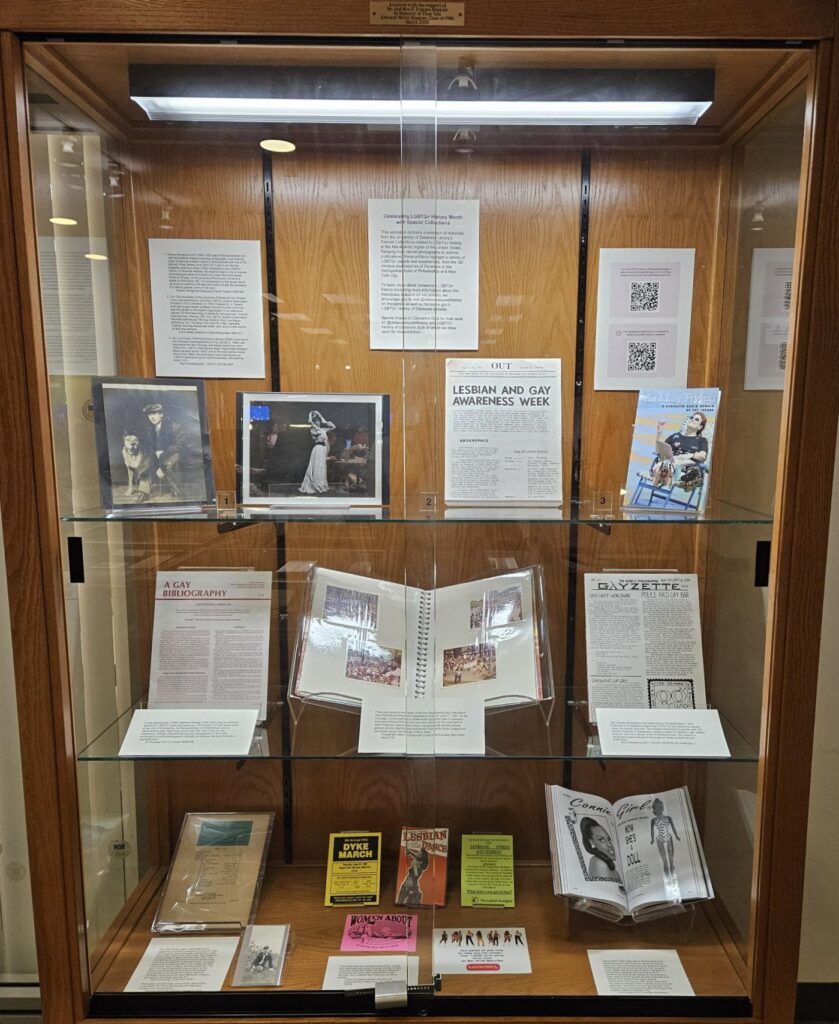 Photograph of an upright wood and glass exhibit case with three shelves of books, papers, and other archival materials.